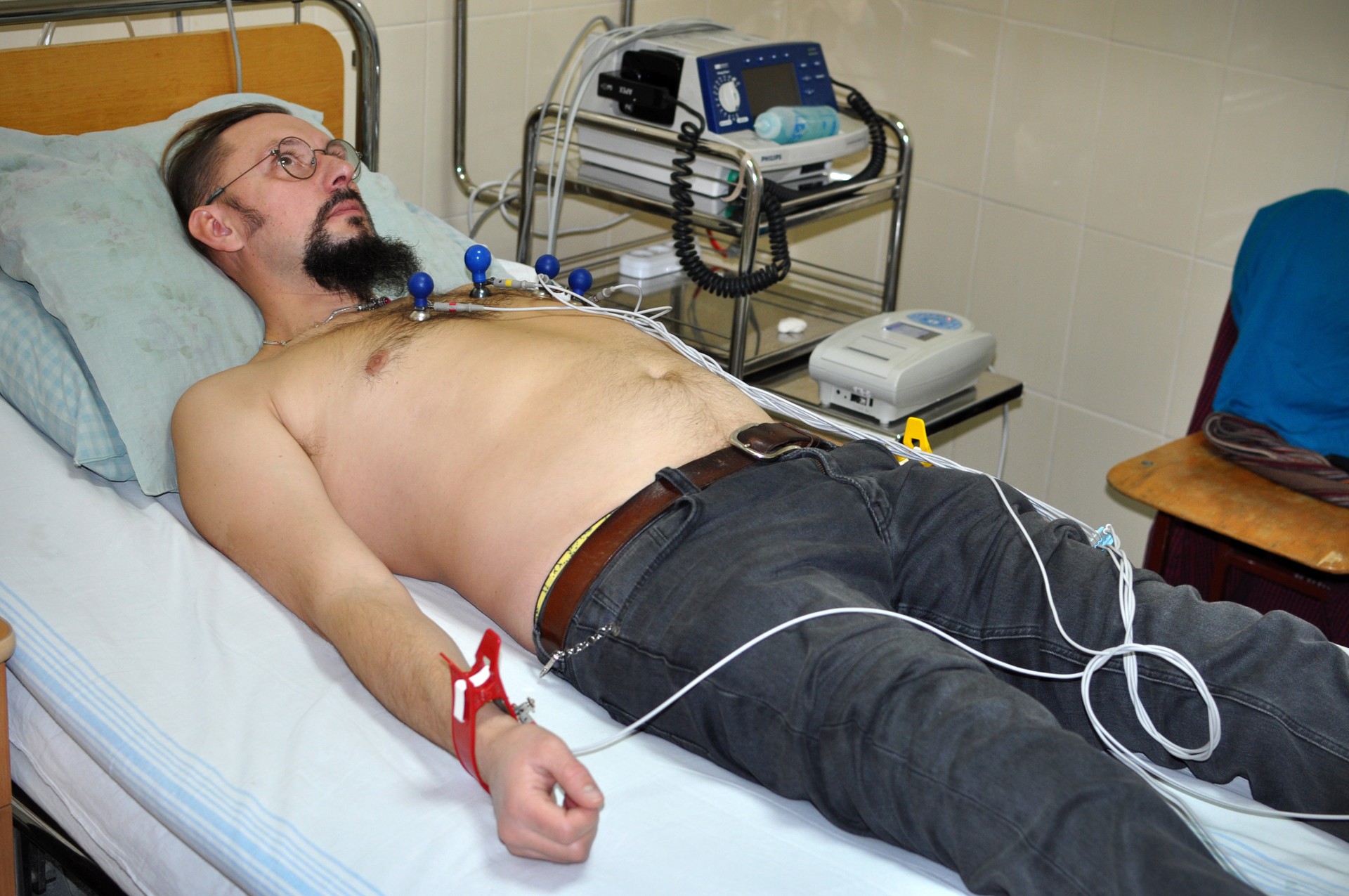 A patient lying on an examination bed with chest electrodes and cables attached for an ECG recording.