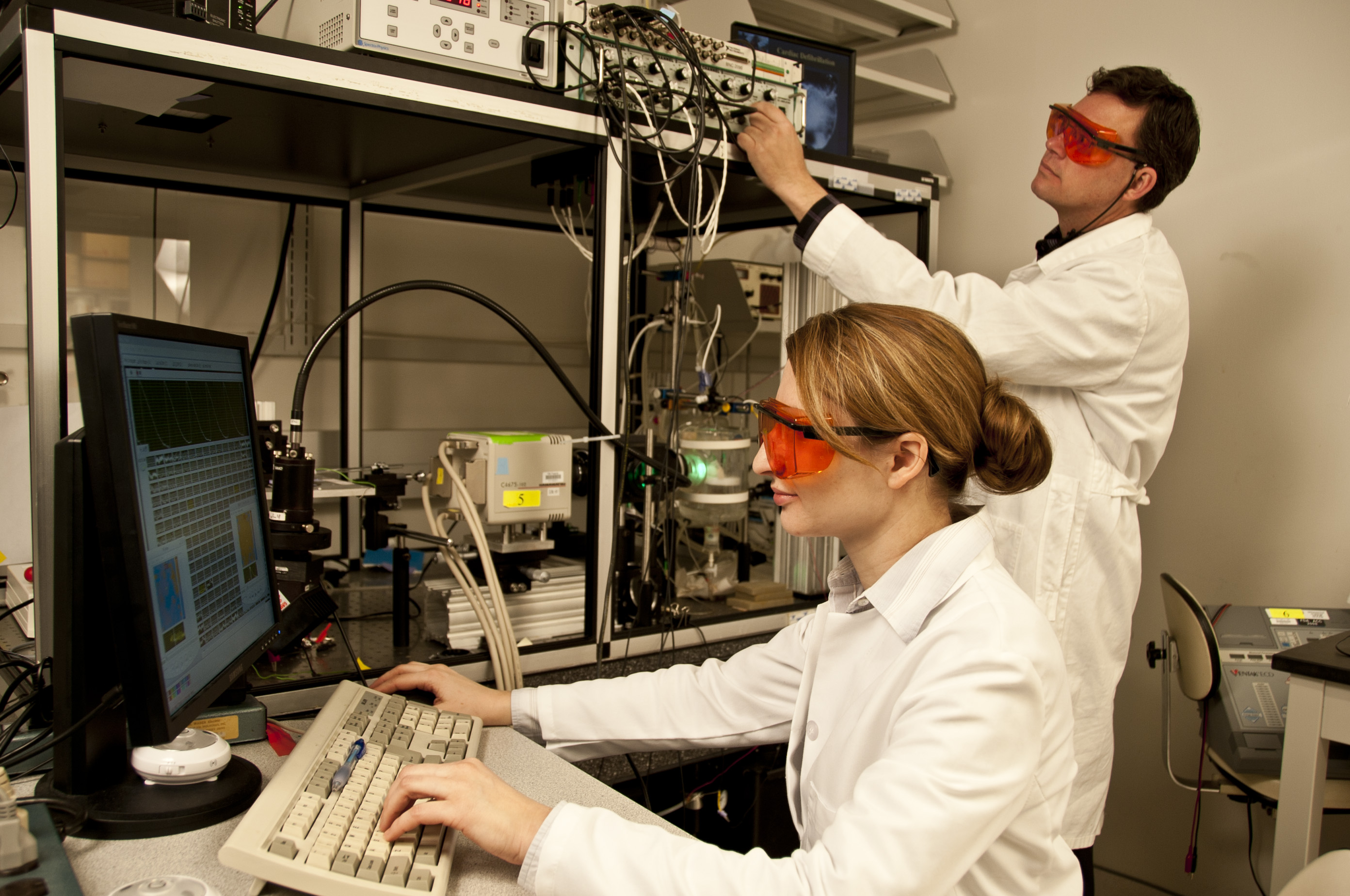 Two FDA researchers wearing protective glasses work with cardiac electrophysiology laboratory equipment.
